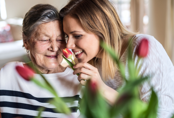 Portrait of an elderly grandmother with an adult granddaughter at home, smelling flowers.