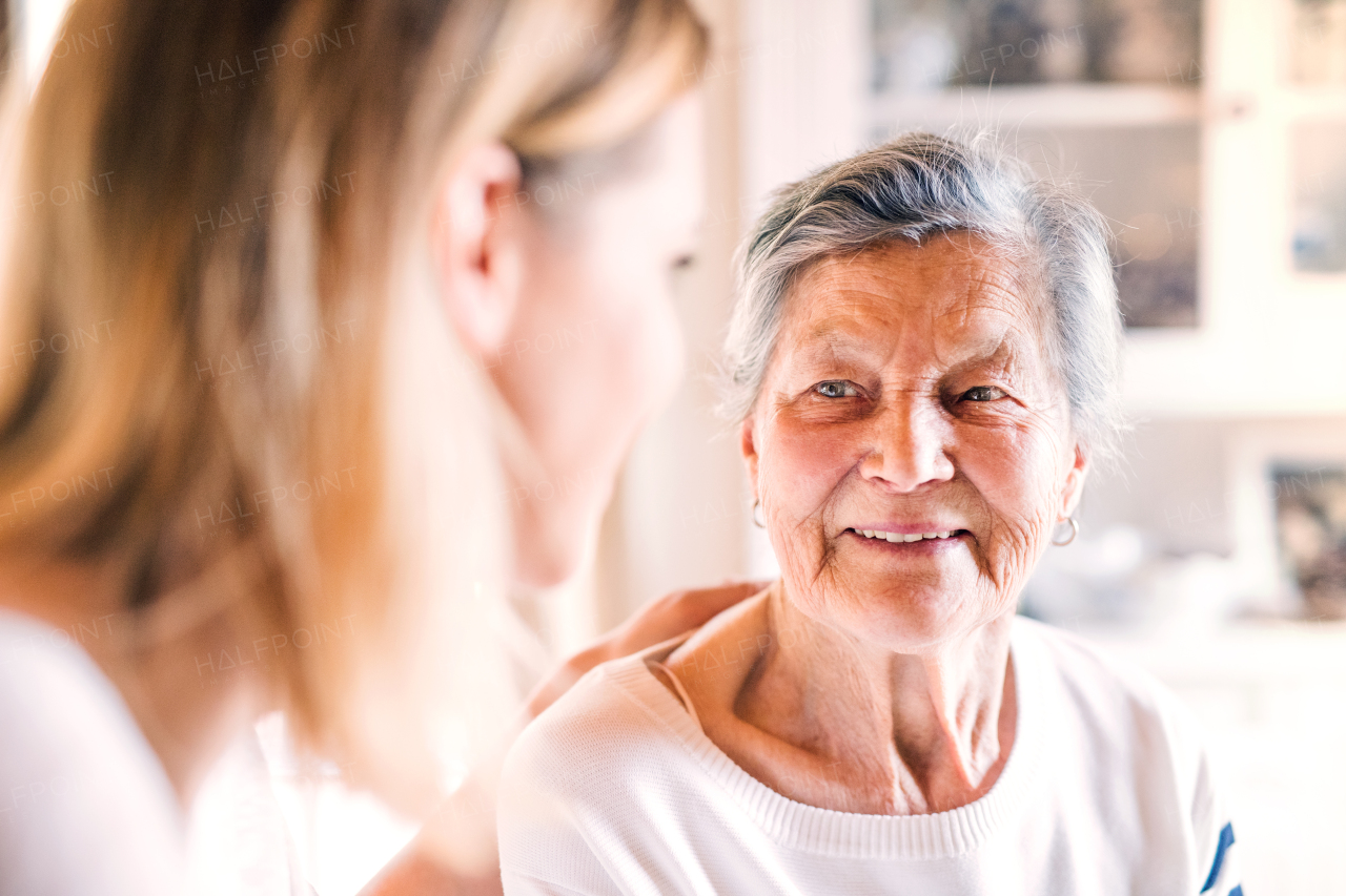 Portrait of an elderly grandmother with an unrecognizable adult granddaughter at home.