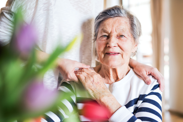 Portrait of an elderly grandmother with an unrecognizable adult granddaughter at home.