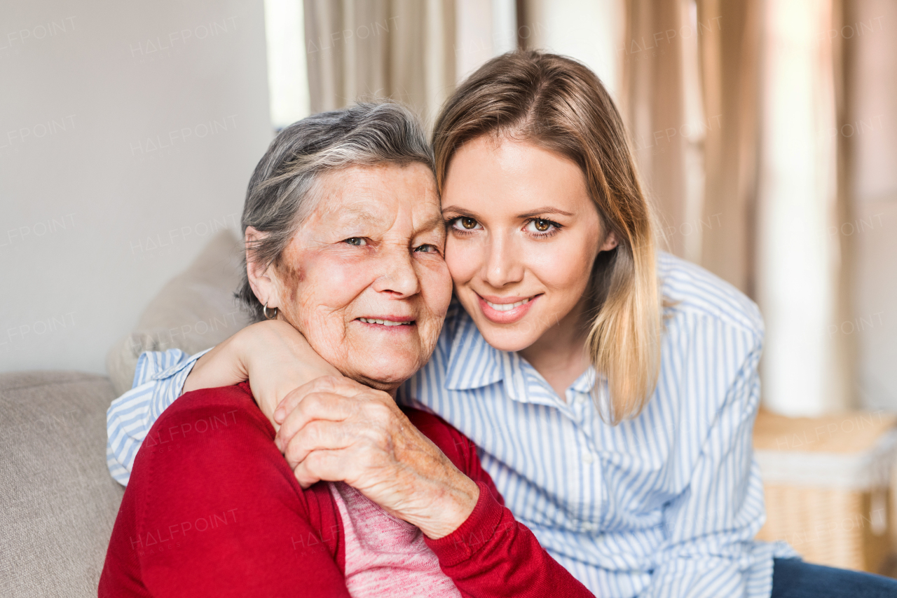 Portrait of an elderly grandmother with an adult granddaughter sitting on the sofa at home.