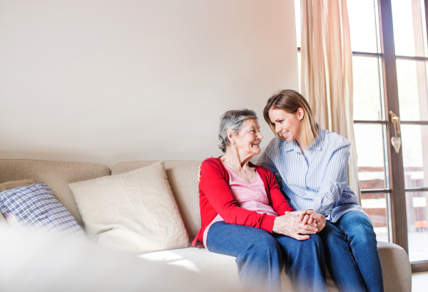 Portrait of an elderly grandmother with an adult granddaughter sitting on the sofa at home.