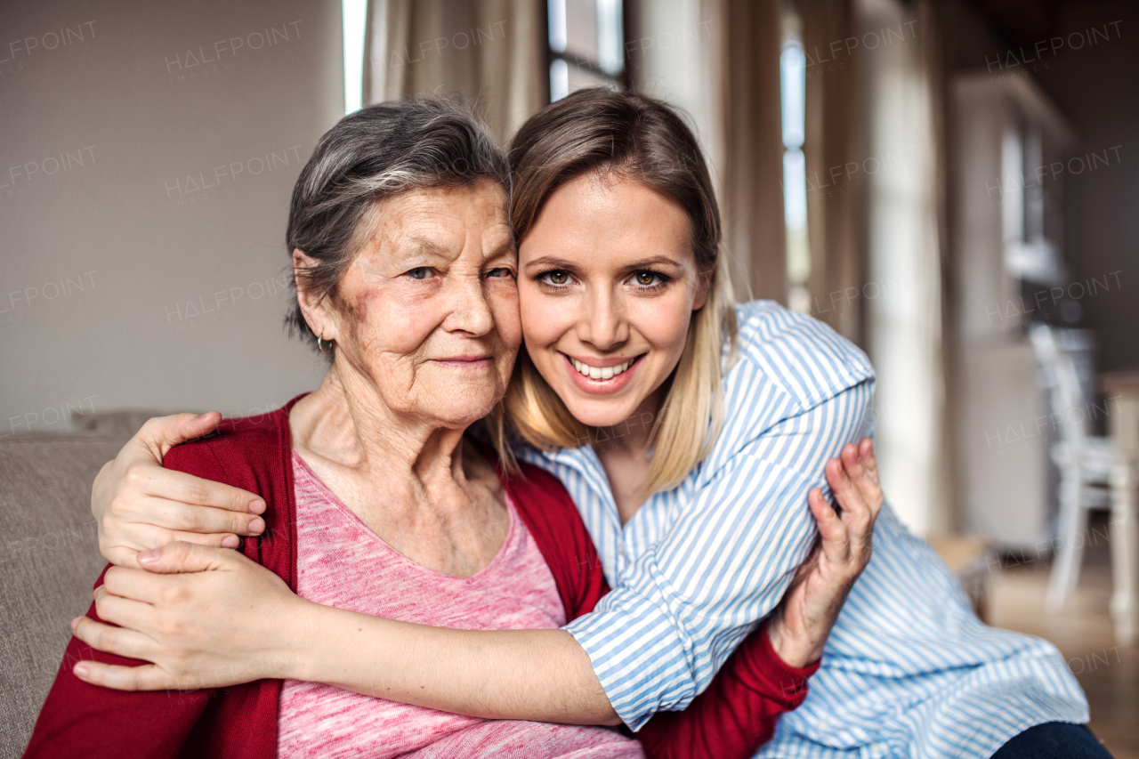 Portrait of an elderly grandmother with an adult granddaughter sitting on the sofa at home, hugging.