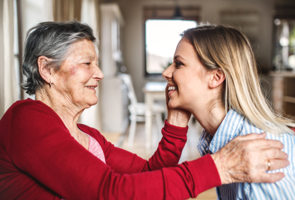 An elderly grandmother looking at and stroking an adult granddaughter at home.