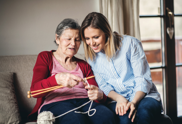 An elderly grandmother teaching and adult granddaughter to knit at home.