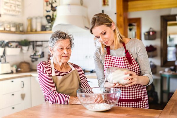 A happy elderly grandmother with an adult granddaughter at home, baking.