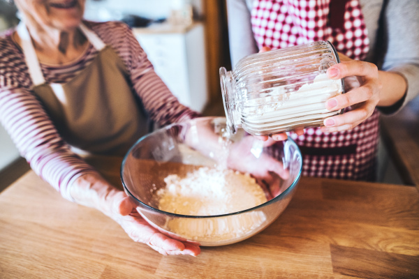 An unrecognizable elderly grandmother with an adult granddaughter at home, baking.