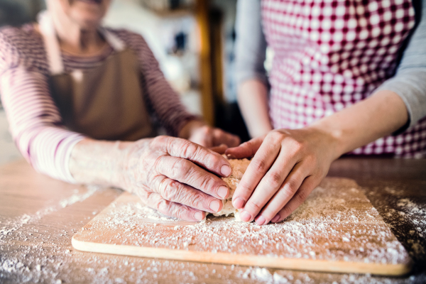 An unrecognizable elderly grandmother with an adult granddaughter at home, baking.