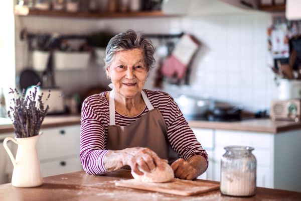 A portrait of a happy senior woman kneading dough in the kitchen at home.