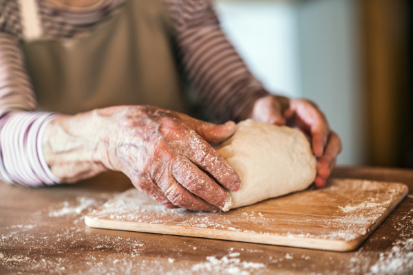 Hands of unrecognizable senior woman kneading dough in the kitchen at home.