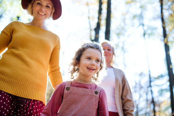 Low angle view of small girl with mother and grandmother on a walk in autumn forest.