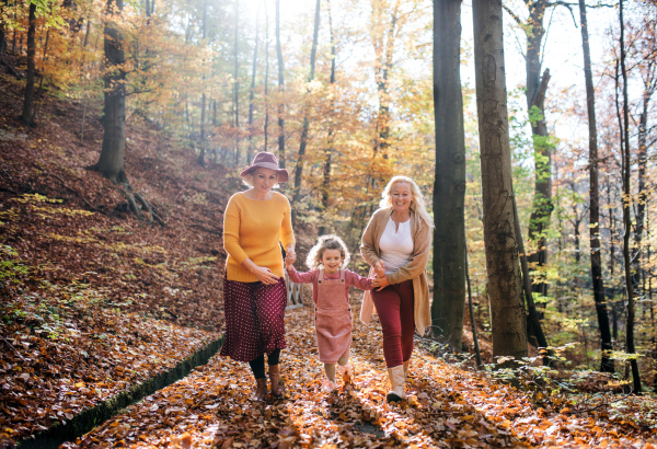 Small girl with mother and grandmother on a walk in autumn forest, running.