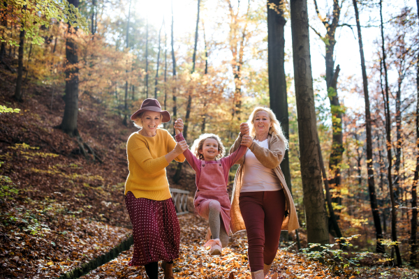 Small girl with mother and grandmother on a walk in autumn forest, having fun.