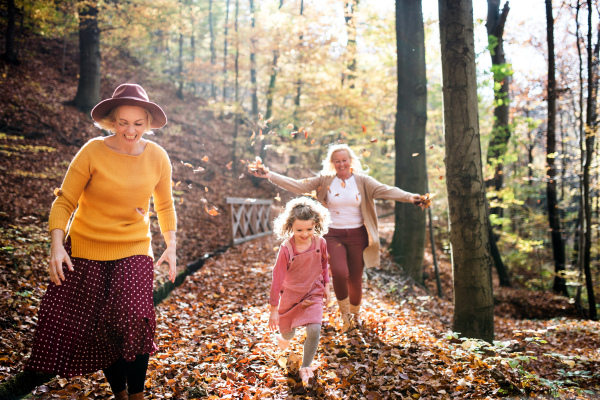 Small girl with mother and grandmother on a walk in autumn forest, having fun.