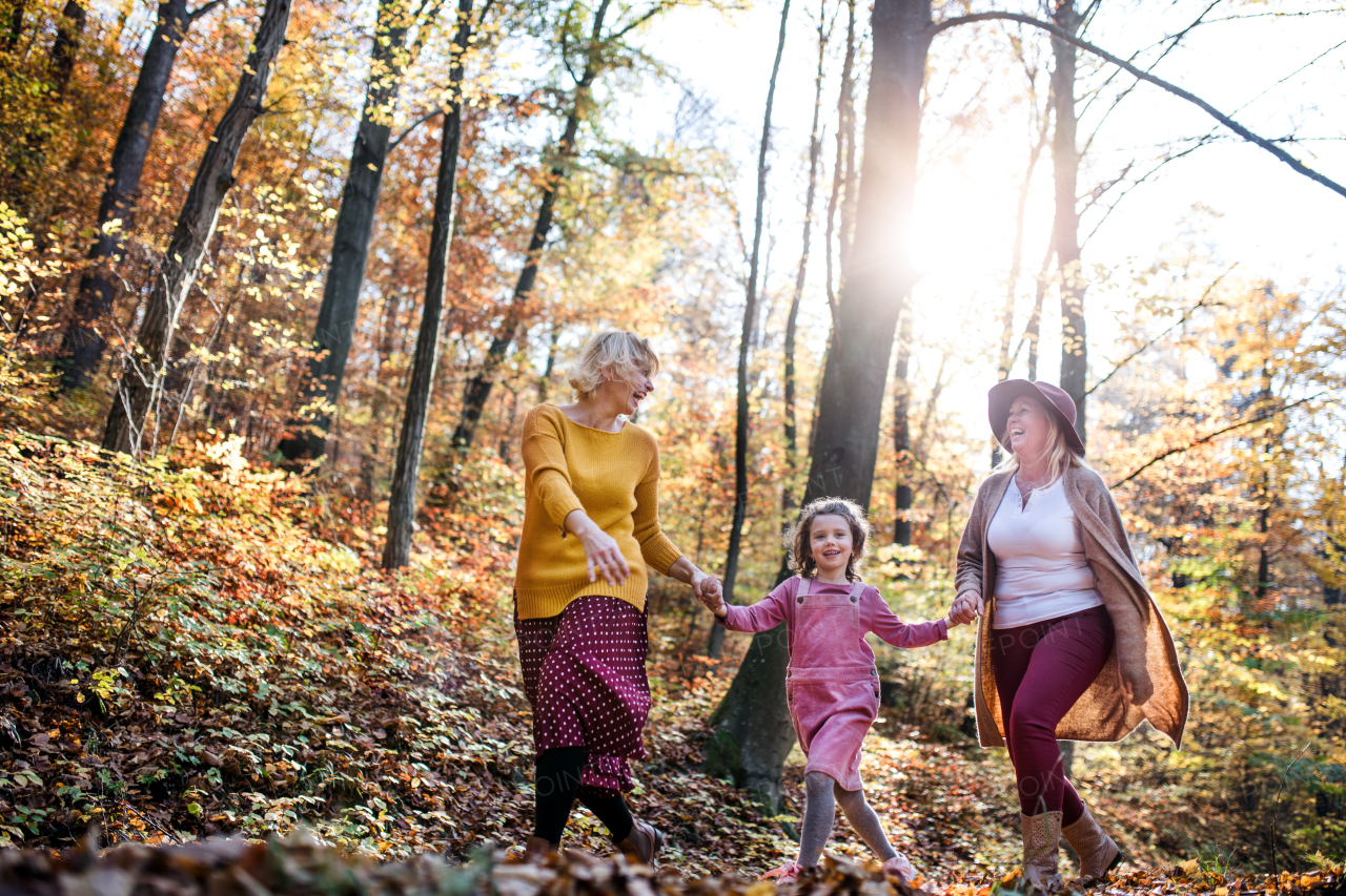 Small girl with mother and grandmother on a walk in autumn forest, talking.