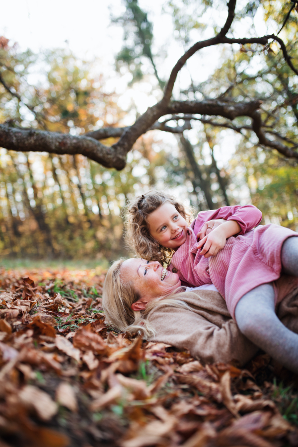 Portrait of small girl with grandmother on a walk in autumn forest, having fun.