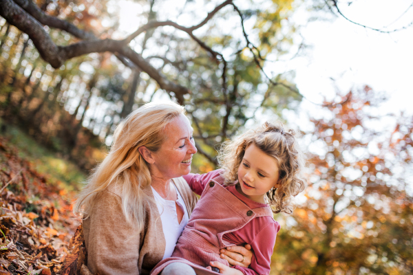 Portrait of small girl with grandmother on a walk in autumn forest, having fun.