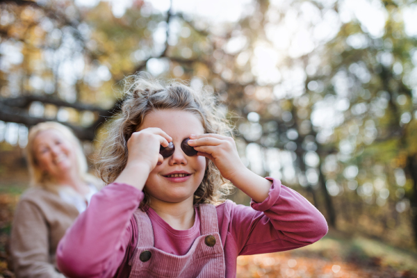 Portrait of small girl with grandmother on a walk in autumn forest, having fun.