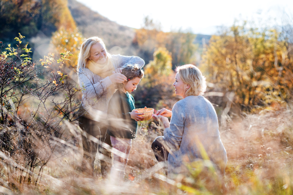 Happy small girl with mother and grandmother collecting rosehip fruit in autumn nature.