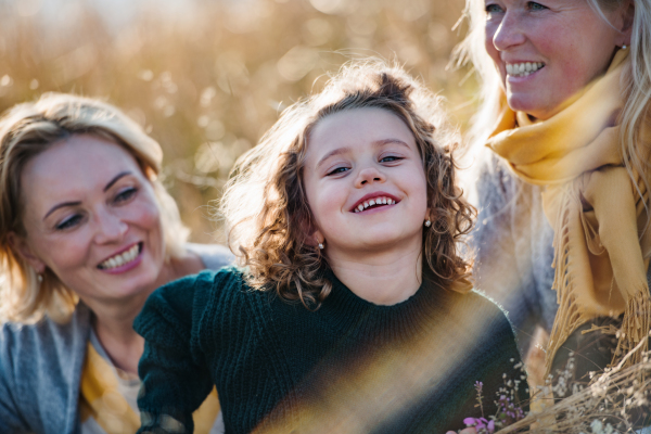 Close-up portrait of small girl with mother and grandmother resting in autumn nature.