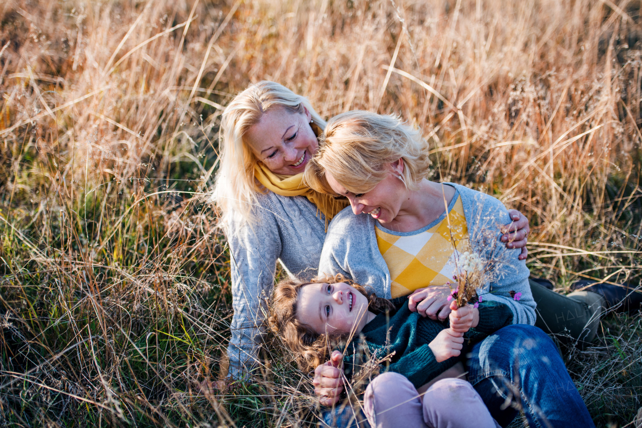 Portrait of cheerful small girl with mother and grandmother resting in autumn nature.