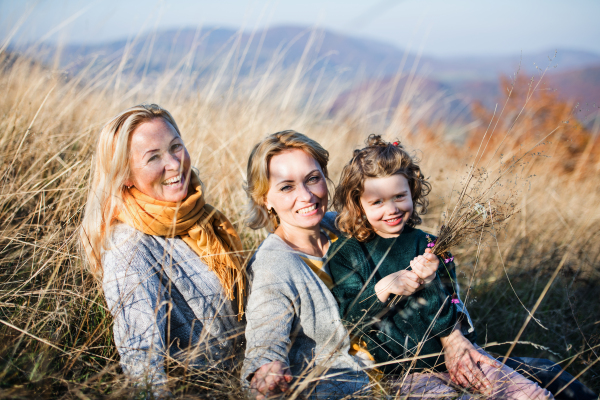 Portrait of small girl with mother and grandmother resting in autumn nature.