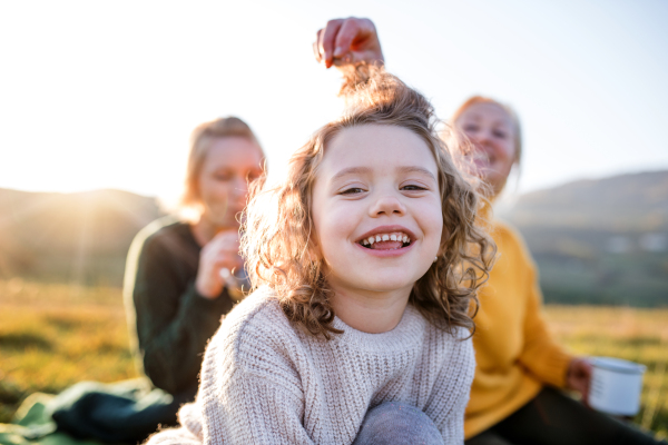 Happy small girl with mother and grandmother having picnic in nature, having fun.