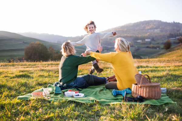 Happy small girl with mother and grandmother having picnic in nature at sunset.