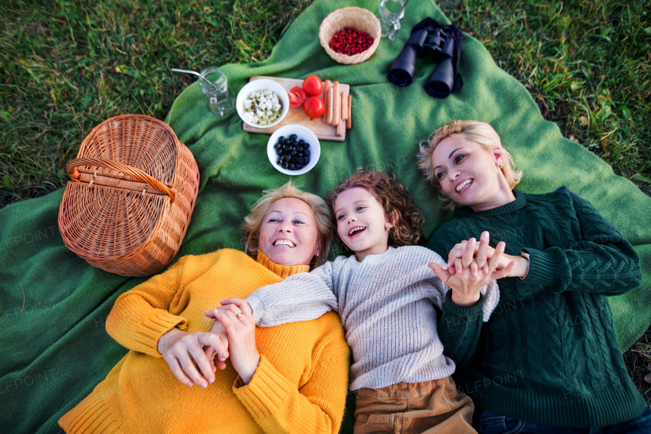 Top view of small girl with mother and grandmother having picnic in nature, laughing.