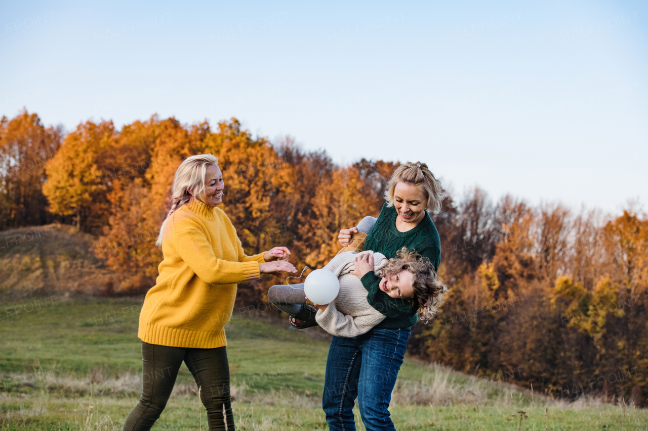 Small girl with mother and grandmother on a walk in autumn nature, having fun.