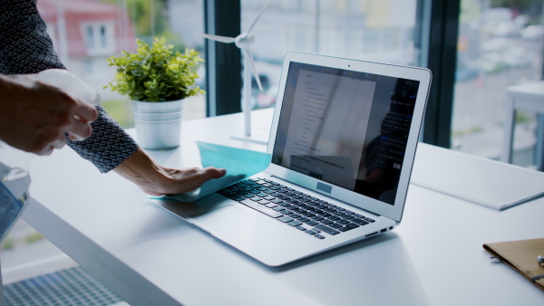 Midsection of unrecognizable woman back at work in office after lockdown, disinfecting laptop.