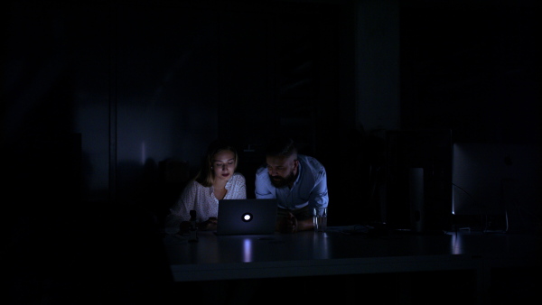 Portrait of business people working late indoors in office at night, talking.