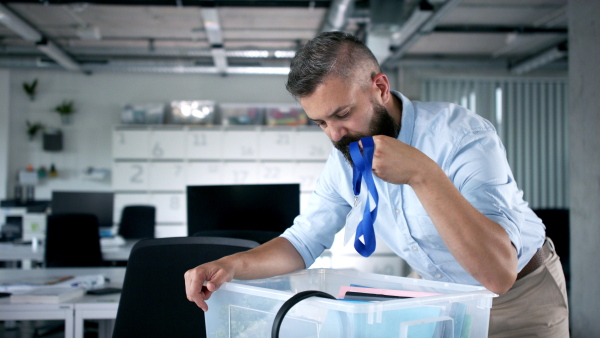 Portrait of sad mature man at desk in office, loosing job due to coronavirus.