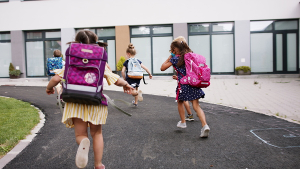 Rear view of group of cheerful children with face masks running outdoors, back to school concept.