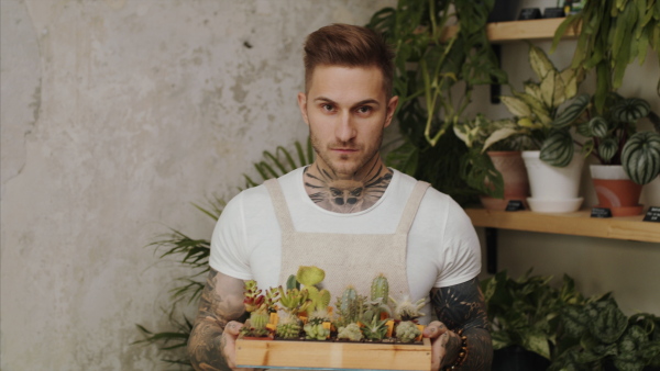 Front view of man florist standing in flower and plant shop, holding succulents.