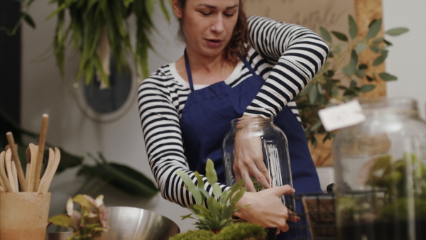 Front view of woman florist in flower and plant shop, making terrarium.