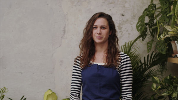 Young woman florist standing in flower and plant shop, looking at camera.