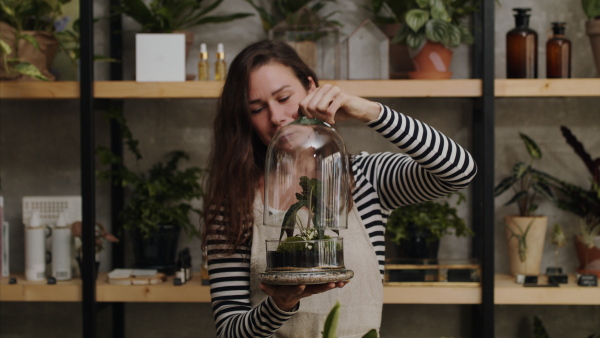 Woman florists with terrarium working in flower and plant shop, looking at camera.