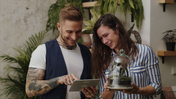 Young man and woman florists with tablet working in flower and plant shop.