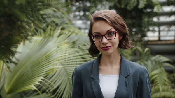 Beautiful young woman standing in botanical garden, looking at camera.