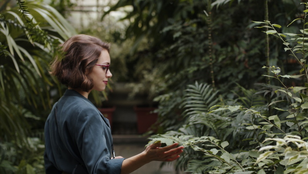 A female researcher standing in botanical garden, exploring plants.