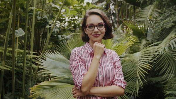 Beautiful young woman standing in botanical garden, looking at camera.