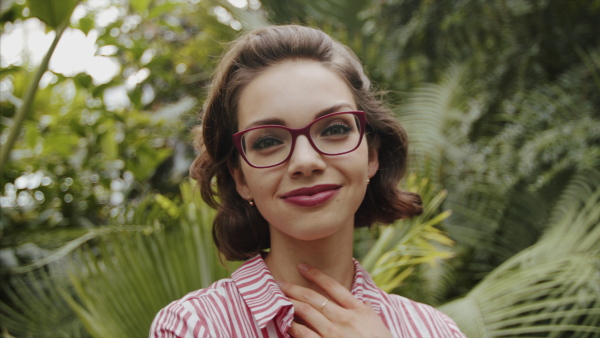 Beautiful young woman standing in botanical garden, looking at camera.