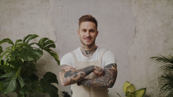 Young man florist standing in flower and plant shop, looking at camera.