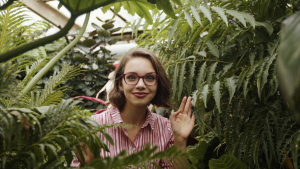 Beautiful young woman walking in botanical garden, looking at camera. Slow motion.