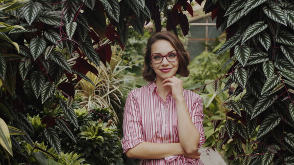 Beautiful young woman standing in botanical garden, looking at camera.