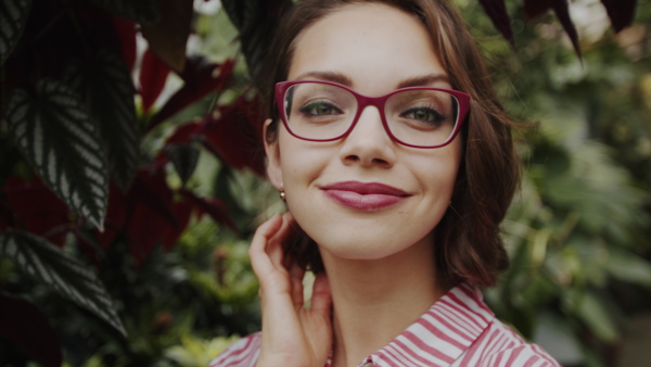 Beautiful young woman standing in botanical garden, looking at camera.