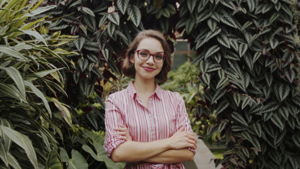 Beautiful young woman standing in botanical garden, looking at camera.