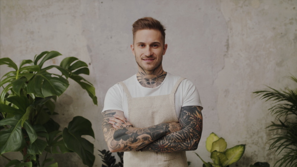 Young man florist standing in flower and plant shop, looking at camera.