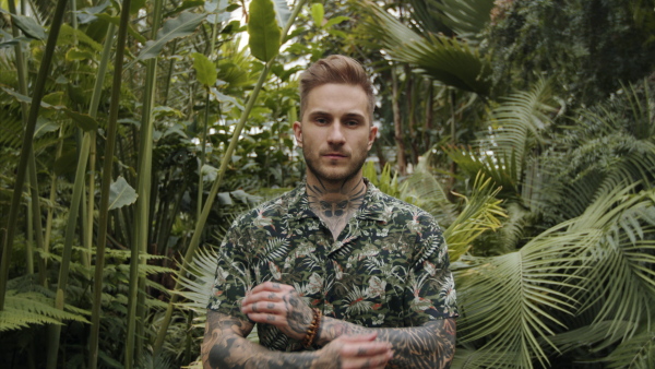 Attractive young man standing in botanical garden, looking at camera.