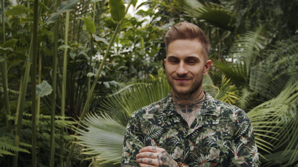 Attractive young man standing in botanical garden, looking at camera.